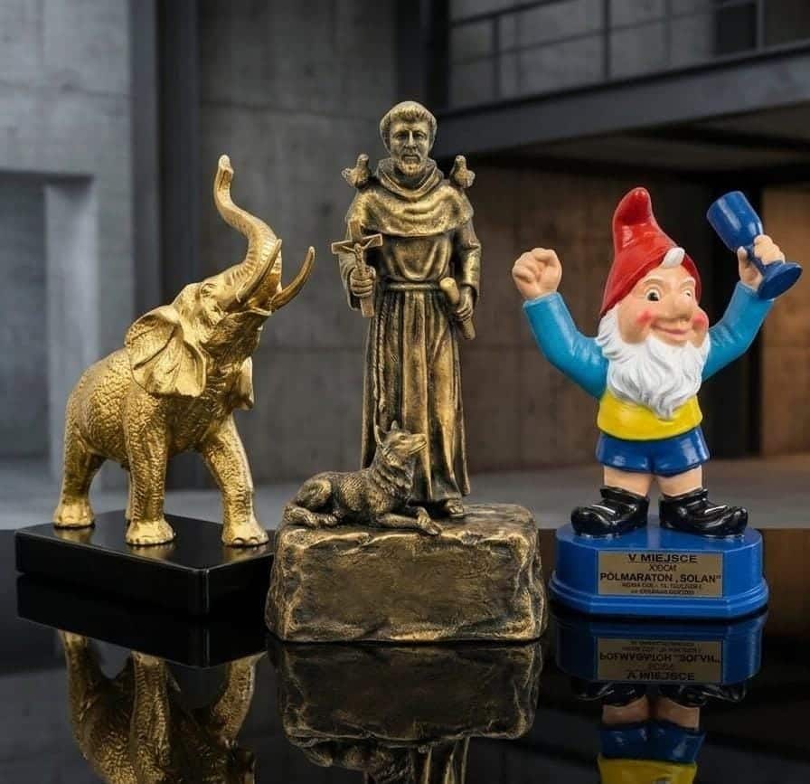 Prestiżowe statuetki biznesowe i nagrody sportowe, w tym złoty słoń oraz trofeum Półmaratonu Solan, ustawione na lustrzanej powierzchni ekspozycyjnej.